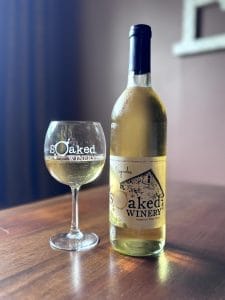 A bottle of vignoles on a table next to a glass of white wine next to it